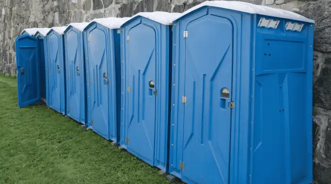 Row of blue portable toilets lined up on grass against a stone wall for event sanitation in Columbus, GA