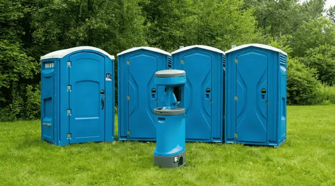 Four blue portable toilets and a matching hand washing station on grass near trees, a common sight at local outdoor events in Columbus, GA