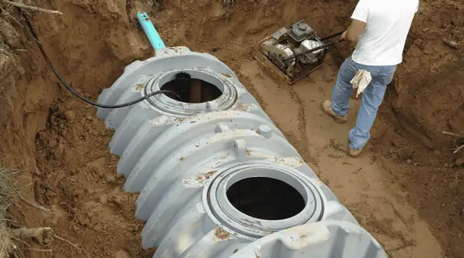 Septic tank installation showing a technician compacting soil around a new poly septic tank in an excavation pit in Columbus, GA